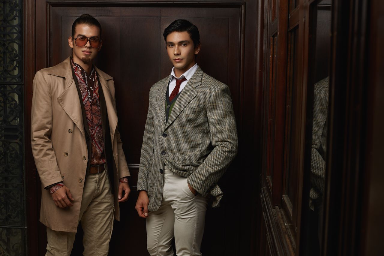 who-we-are Two men in fashionable suits posing indoors, showcasing elegance and style.