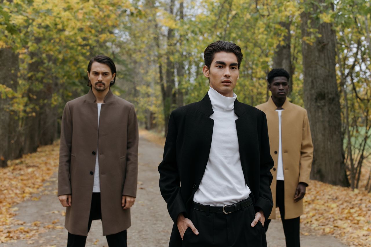 services-04 Three men in stylish coats standing on a leafy path in autumn.